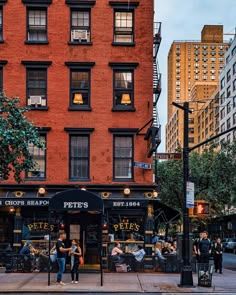 people are sitting at tables on the sidewalk in front of a brick building with many windows