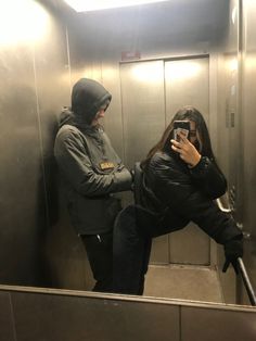 a woman taking a selfie in an elevator while another person takes a photo with their cell phone