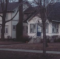 a white house with trees and bushes in front of it on a gloomy day