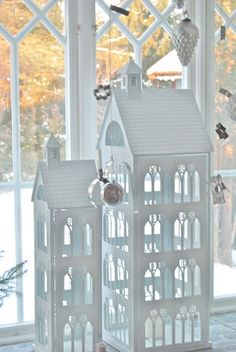 two white houses sitting on top of a table next to a window with birds flying over it