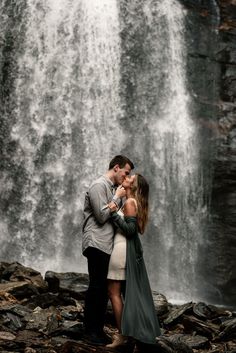 a man and woman standing in front of a waterfall