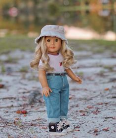 a doll with blonde hair wearing a hat and blue jeans standing in the dirt on a sunny day