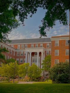 a clock on a pole in front of a large brick building with columns and pillars