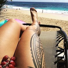 a woman laying in a chair on the beach with her legs crossed and tattooing