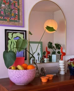 a bowl of fruit sits on a dresser in front of a mirror and art work