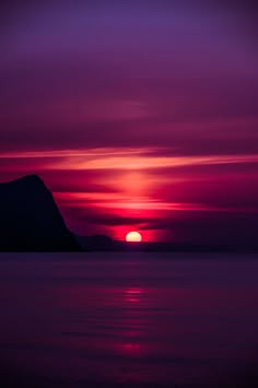 the sun is setting over water with mountains in the background