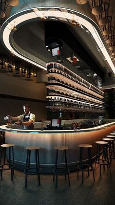 a bar with lots of stools in front of it and a man sitting at the bar