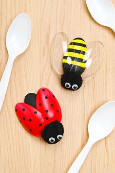 two plastic ladybugs sitting next to spoons on top of a wooden table