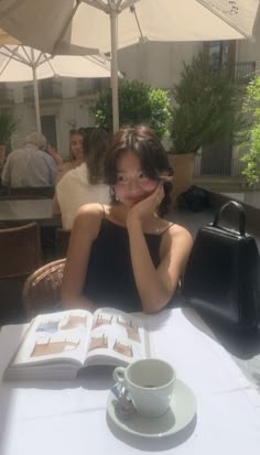 a woman sitting at a table with an open book and coffee cup in front of her