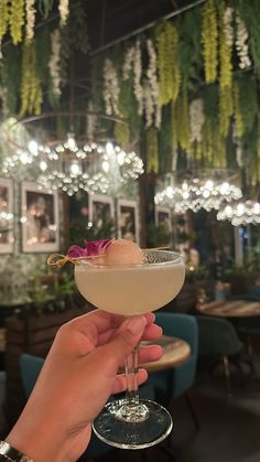 a person holding up a wine glass in front of a chandelier filled with flowers