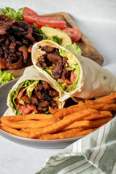 two wraps with meat, lettuce and carrots on a plate next to some fries