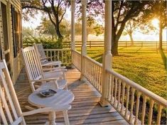 two white rocking chairs sitting on top of a wooden porch next to a tree filled field