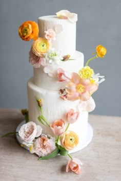 a three tiered white cake with flowers on the top and bottom, sitting on a table