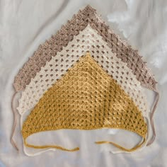 three crocheted triangle hats on top of a white cloth covered bedding sheet