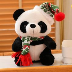 a stuffed panda bear wearing a christmas hat and scarf sitting on a table next to a cup