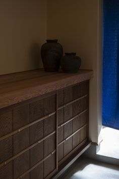 two vases sitting on top of a wooden shelf in front of a blue curtain