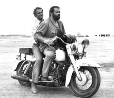 two men riding on the back of a motorcycle in black and white, one with a beard