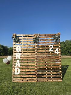 a wooden sign that says grand on it in front of some balloons and grass with trees