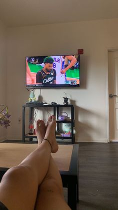 a person is sitting in front of a tv watching sports on the television screen while holding their feet up