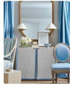 a blue chair sitting in front of a mirror next to a table with flowers on it