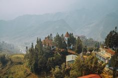 a train is traveling down the tracks near some houses and mountains in the distance with trees on both sides