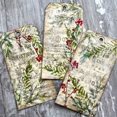 three tags with holly and berries on them sitting on top of a wooden table next to each other