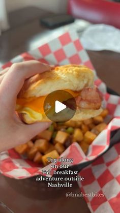 a person is holding a sandwich with eggs and bacon on it while sitting at a table