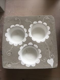 three white bowls sitting on top of a cement block with flowers painted on it and hearts drawn on the side