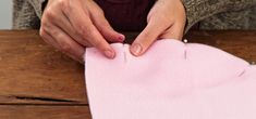 a woman is making a pink piece of fabric on a wooden table with her hands