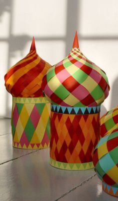 three brightly colored baskets sitting on top of a wooden table next to each other, with shadows from the wall behind them