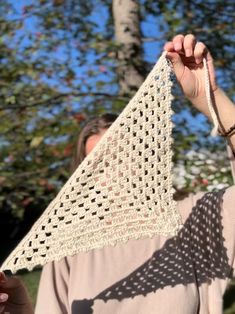 a woman holding up a triangle shaped piece of crocheted material in front of her face