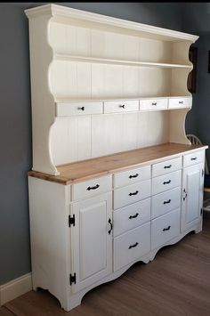 a large white cabinet with drawers and cupboards on the top, next to a chair