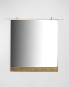 a mirror hanging on the wall with a gold frame and metal bar at the bottom