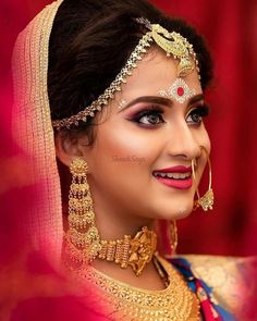 a woman wearing a red and gold bridal outfit with jewelry on her head, in front of a red background