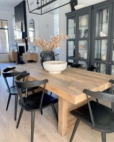 a dining room table with black chairs and a vase on top of it in front of a china cabinet