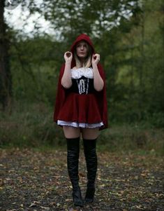 a woman in a red cape and black boots is standing on the ground with her hands behind her head