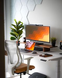 a desk with a computer, chair and potted plant in front of the monitor