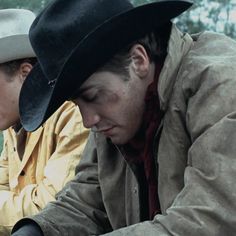 two men in cowboy hats are looking at something on a piece of paper while sitting next to each other