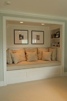 a window seat with pillows and pictures on the wall above it in a living room