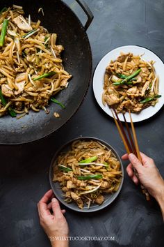 someone holding chopsticks over a wok filled with stir fried noodles and vegetables