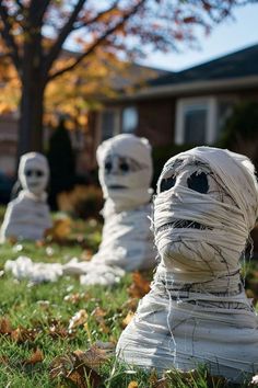 three fake heads wrapped in white paper sitting on the grass next to a tree and house