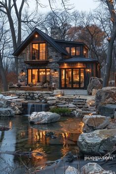 a house that is surrounded by rocks and trees with lights on the windows in front of it