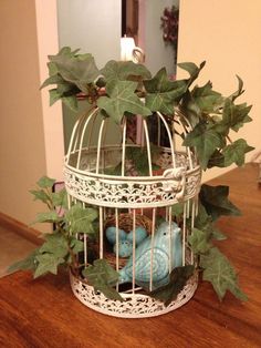 a bird in a cage with ivy growing on the outside and inside, sitting on a table