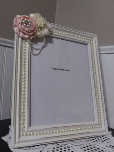 a white frame with pearls and a pink flower