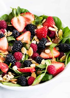 a white bowl filled with spinach, berries and almonds on top of a table