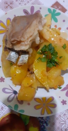 a white plate topped with meat and fruit on top of a floral tablecloth covered table