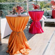 two tables with orange and pink cloths on them, one has flowers in a vase