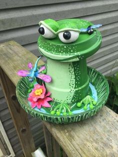 a green frog statue sitting on top of a wooden bench next to a flower pot