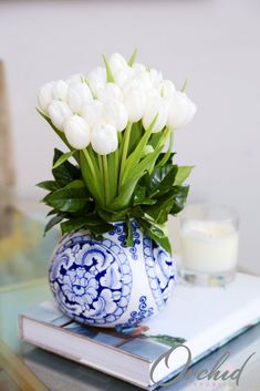 white tulips in a blue and white vase on top of a stack of books