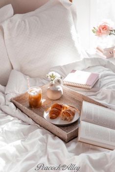 an open book and two cups on a tray with food sitting on top of a bed